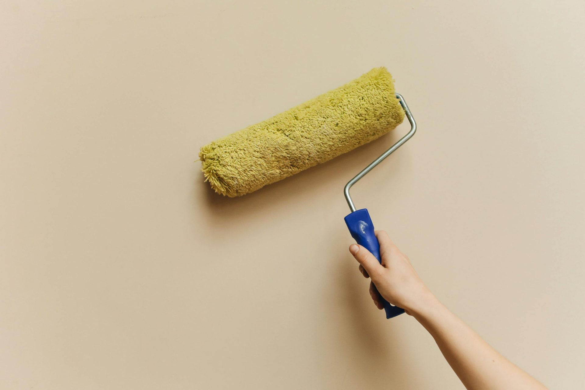 Eine Hand streicht mit einer gelben Farbrolle eine beige Wand. Perfekt für Heimwerker- und Renovierungsprojekte.