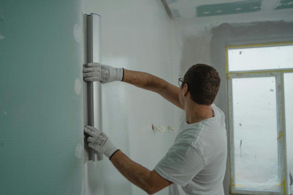 Ein Mann in weißem Hemd und Handschuhen benutzt ein Metalllineal für Renovierungsarbeiten an Innenwänden.